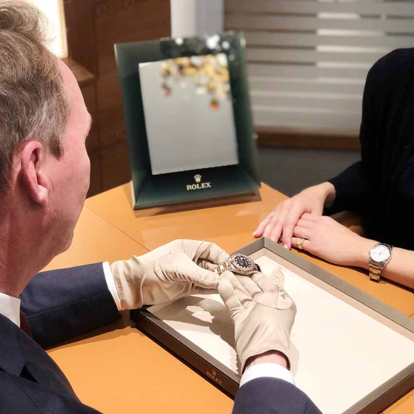 Im Rolex Showroom von Juwelier Freisfeld präsentiert ein Mitarbeiter mit Handschuhen einer Kundin eine Rolex Uhr