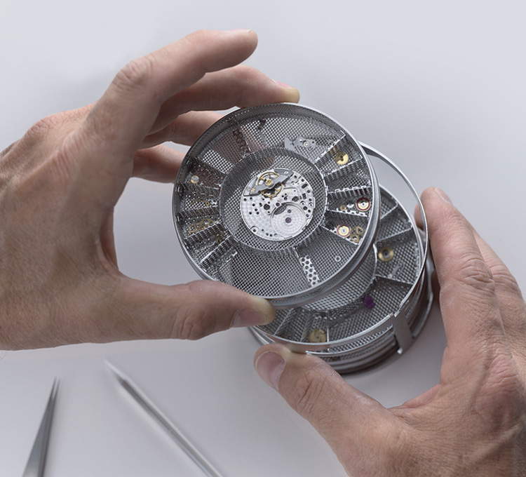 Ein Mann stapelt Kleinteile für das Werk einer Rolex Uhr in einem Metallbehälter